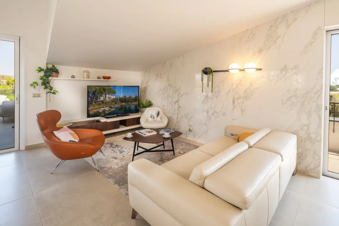 Modern living room with beige sofa, brown leather armchair, coffee table, and television displaying a landscape