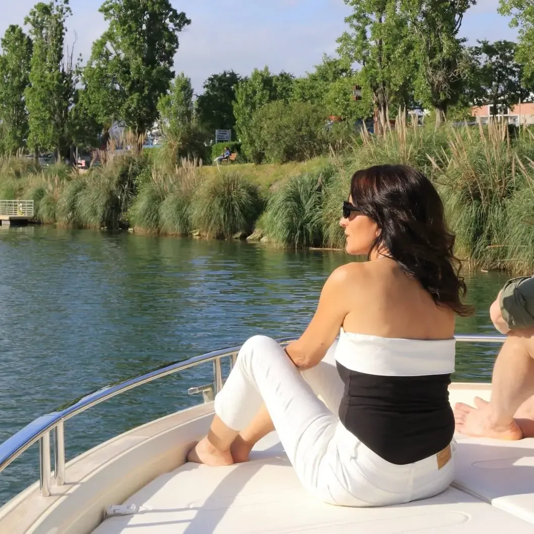 A man and a woman sitting at the front of a boat on a body of water surrounded by vegetation and buildings.