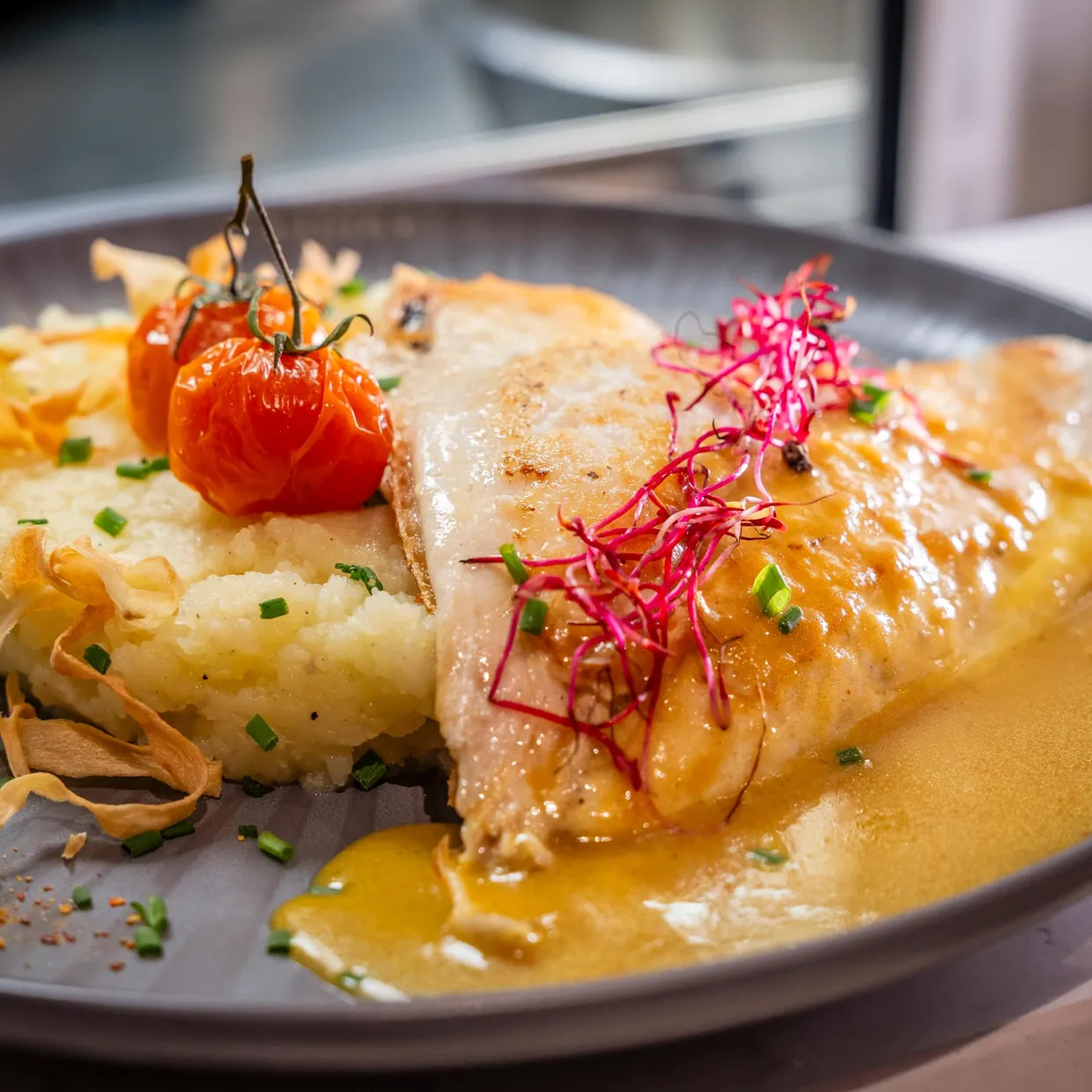 A grilled fish fillet served on a purée, accompanied by cherry tomatoes, radishes, and vegetable chips.