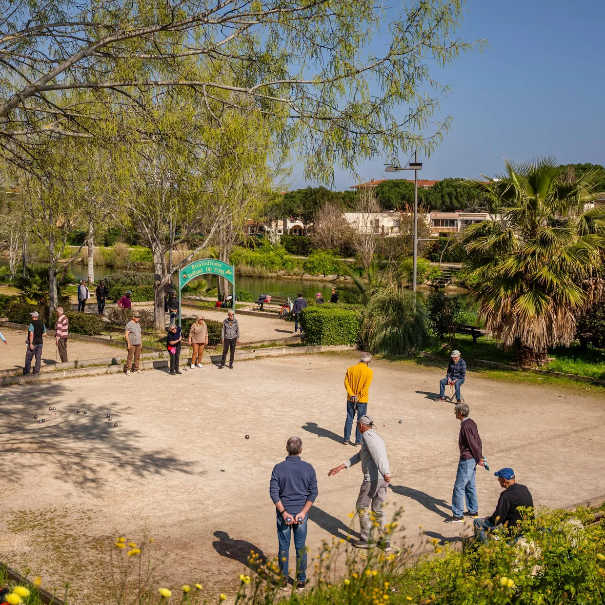 Un groupe de personnes joue à la pétanque dans un parc arboré près d'un plan d'eau