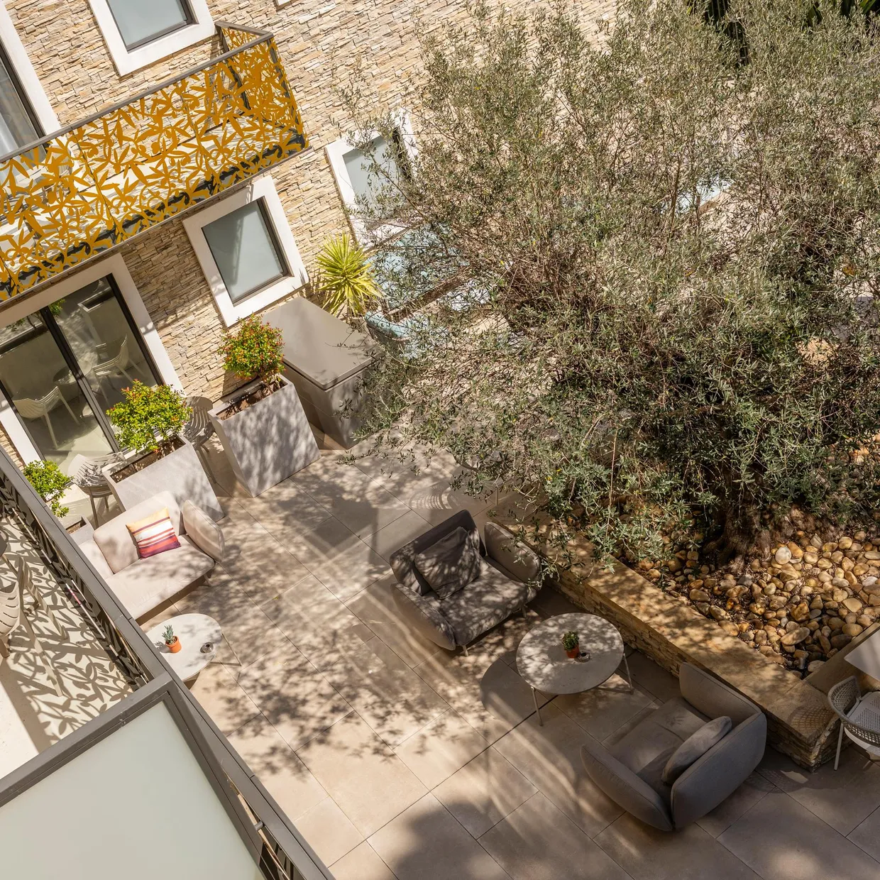 Terrace with garden furniture, including a table, chairs, and sofa, surrounded by vegetation and brick walls with decorative patterns.