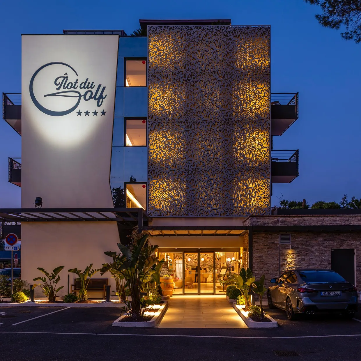 Four-star "Plat du Golf" hotel with illuminated facade and entrance accessible via a paved path
