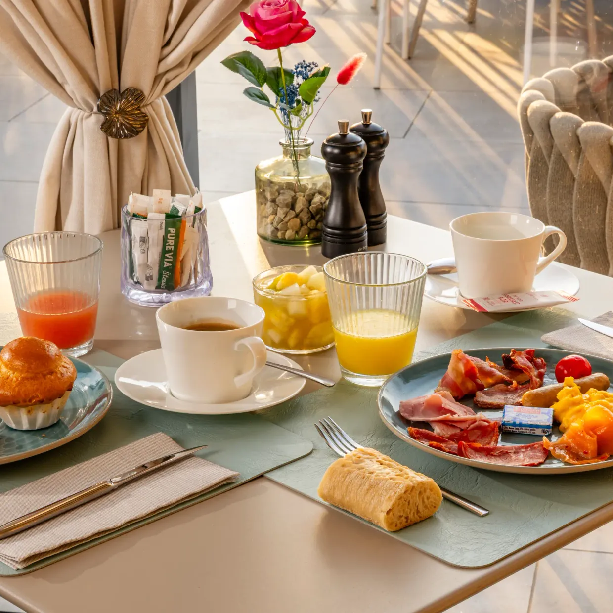 Table set for breakfast with croissants, muffins, eggs, ham, cheese, drinks, and condiments.