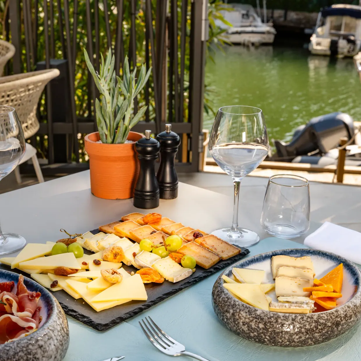 Table with charcuterie platter, cheeses, glasses, and view of a canal with boats