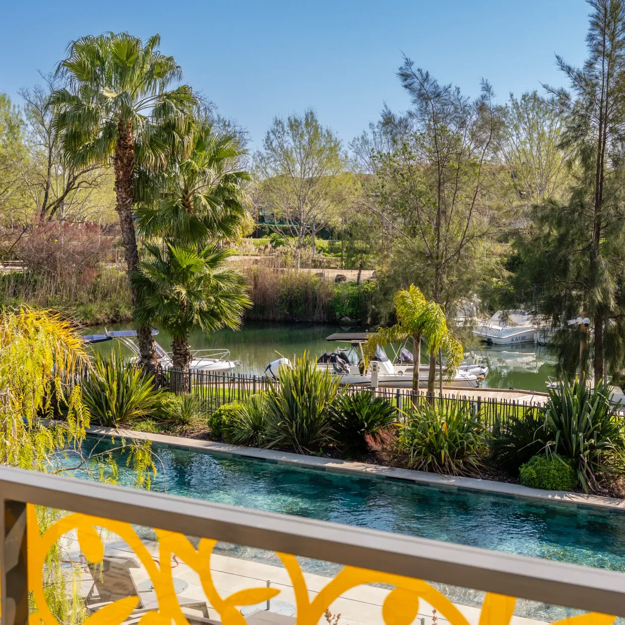 View of a lake with moored boats, surrounded by trees and vegetation, from a balcony with a pool in the foreground
