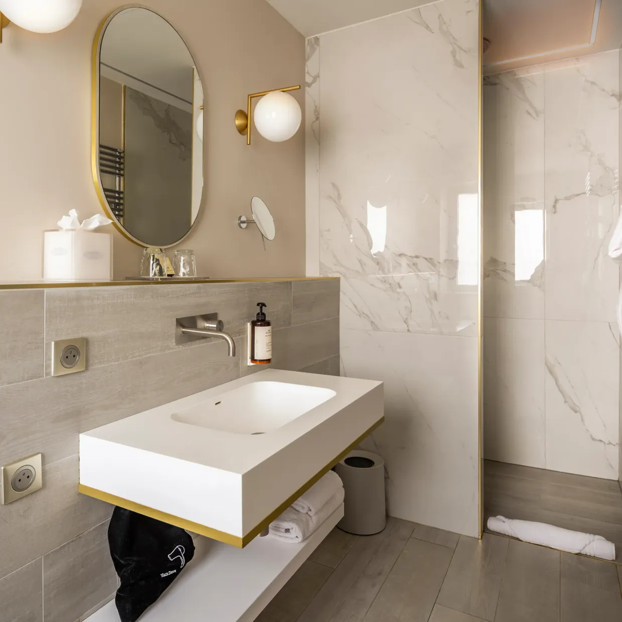 Modern bathroom with suspended sink, oval mirror, glass-doored shower, and hanging towels
