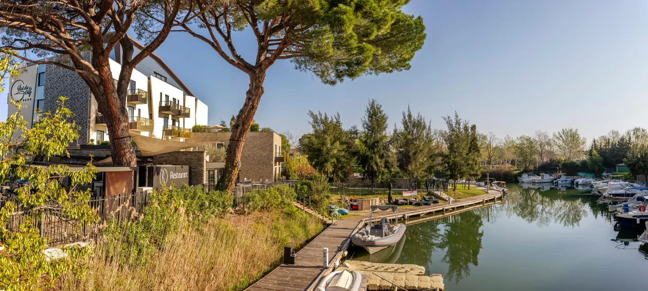 A hotel and a restaurant overlook a canal with moored boats, surrounded by trees and vegetation.