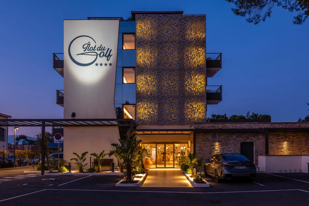 Four-star "Plat du Golf" hotel with illuminated facade and entrance accessible via a paved path