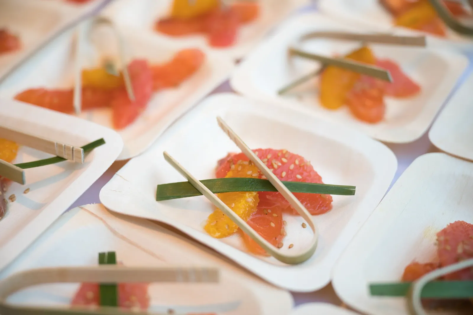 Small cardboard containers holding pieces of fruit and sticks, arranged on a patterned tablecloth