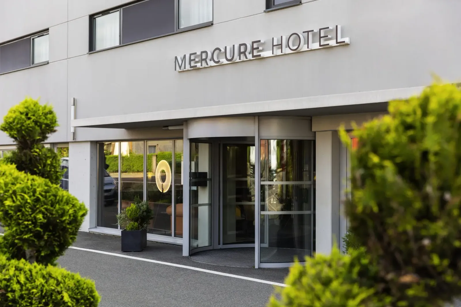 Main entrance of a Mercure hotel with potted plants and glass windows