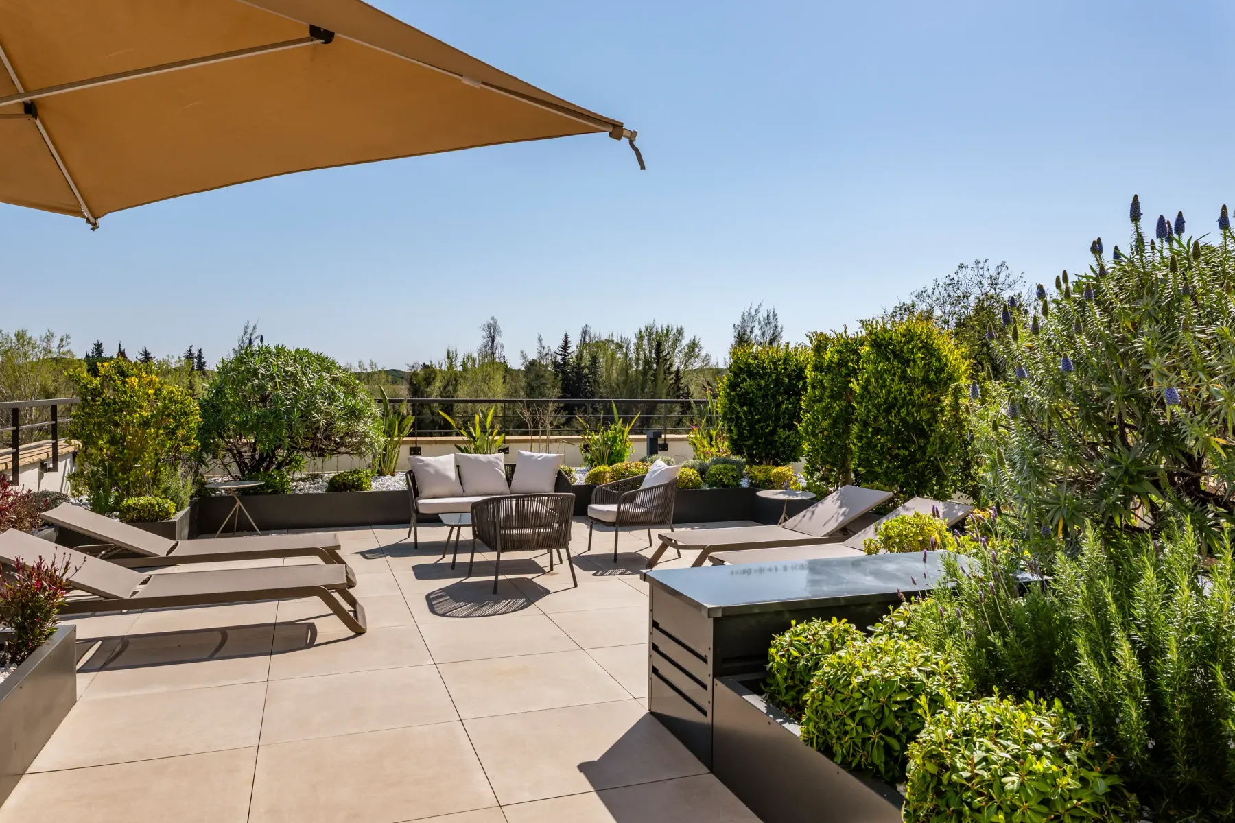 Terrace with sun loungers, a sofa, plants, and an umbrella under a clear sky
