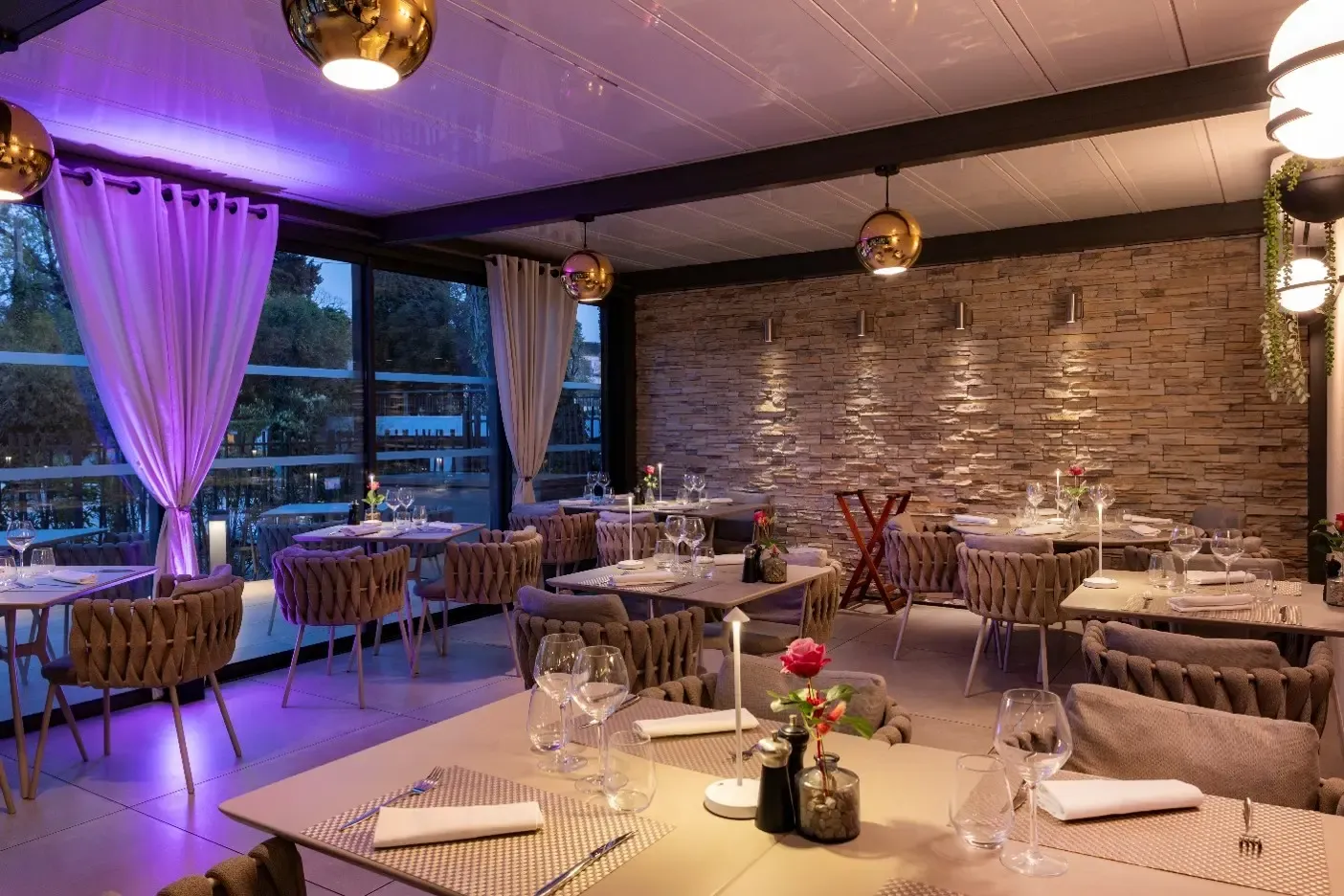 Elegant restaurant with set tables, padded chairs, and dim lighting, offering an outdoor view through large windows.