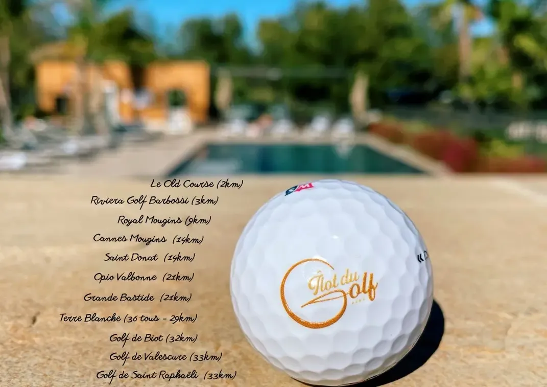 Golf ball with the inscription "Golf du Domaine" in front of a swimming pool and buildings in the background