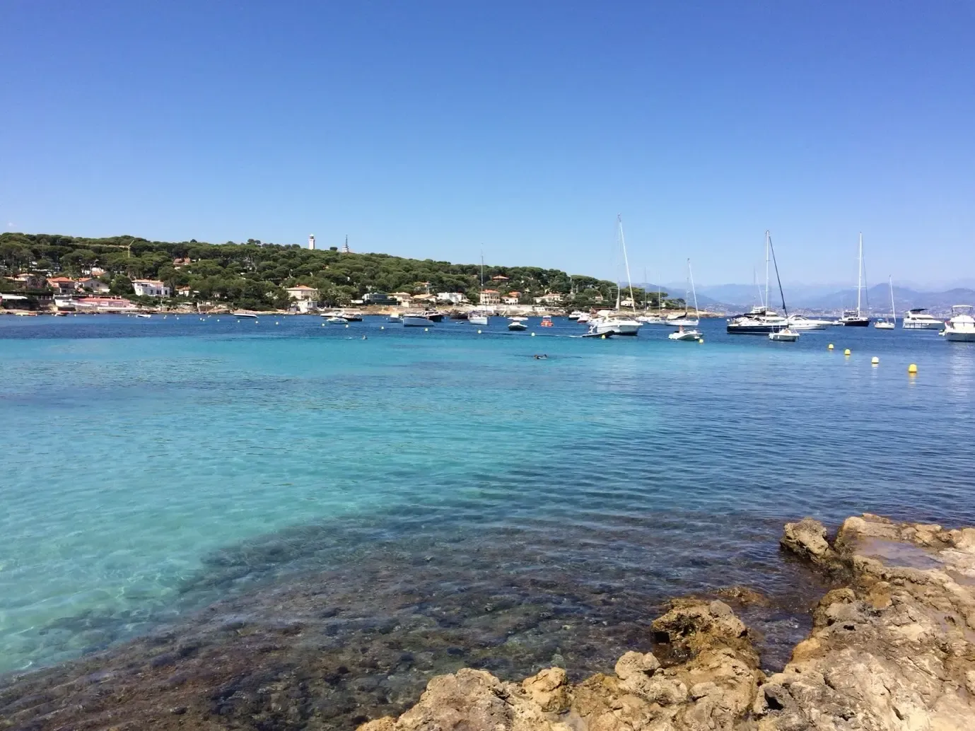 View of a bay with turquoise waters, sailboats, and a coastal village in the background