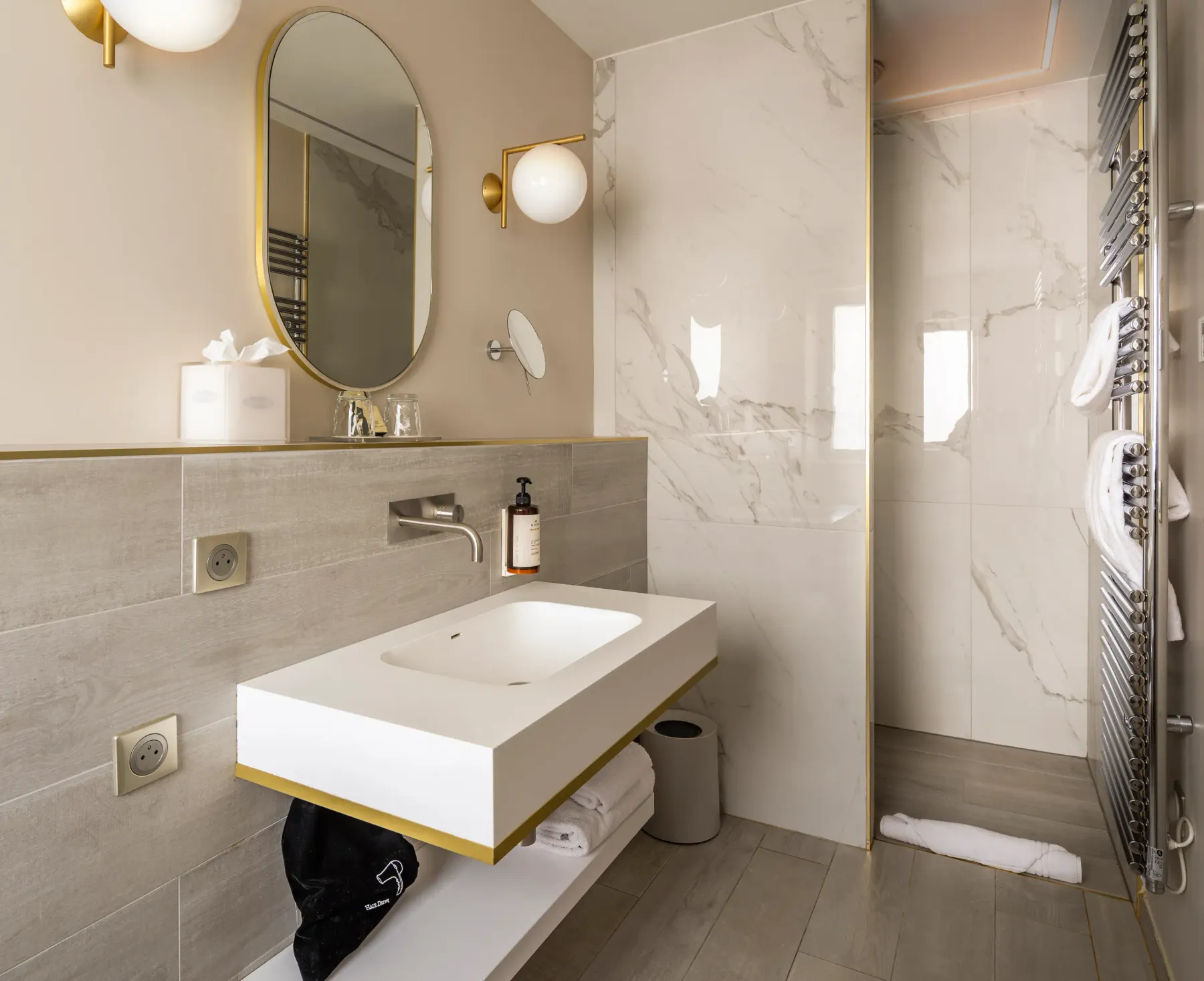 Modern bathroom with suspended sink, oval mirror, glass-doored shower, and hanging towels