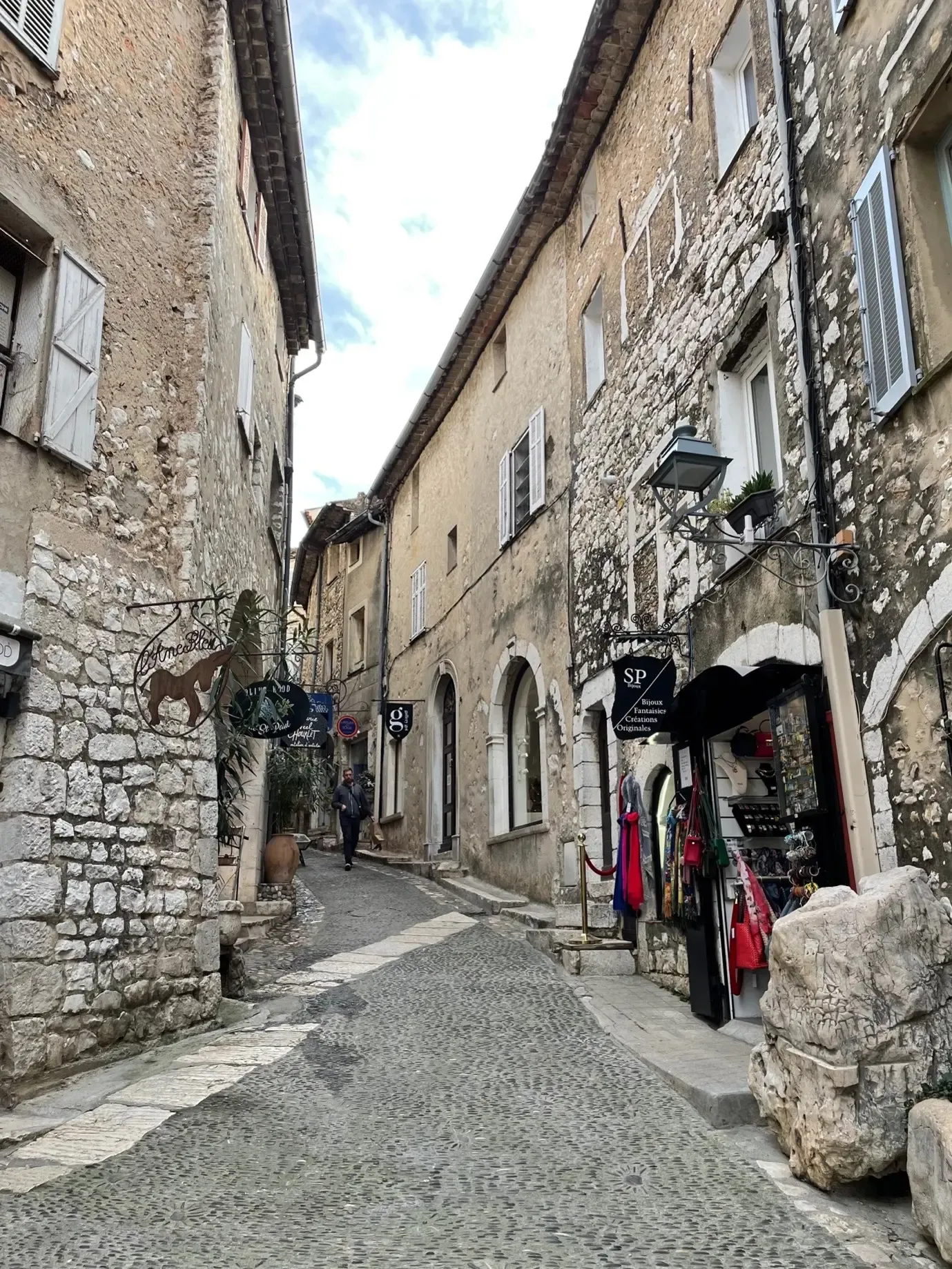 Cobbled alley flanked by stone buildings with shops and a person walking in the distance
