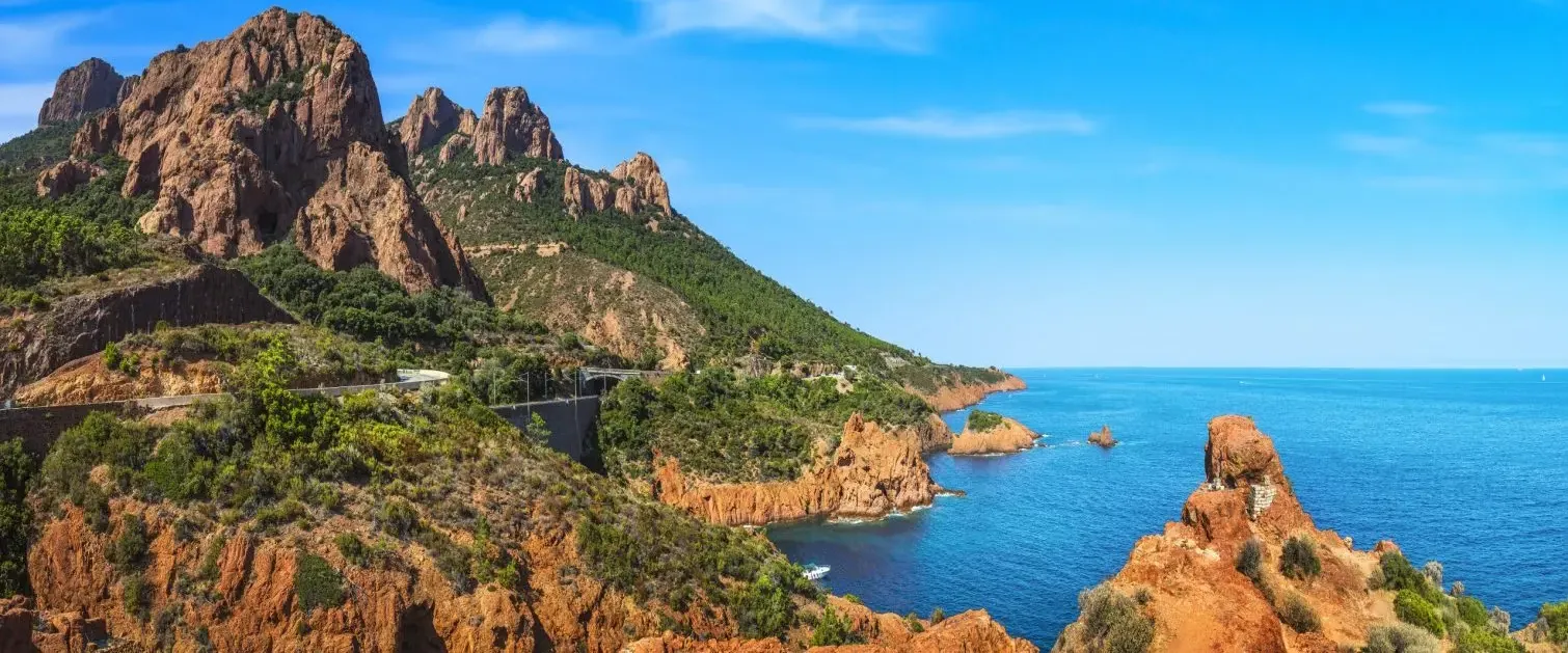 A rocky coastline with steep mountain formations and a winding road along the blue sea under a clear sky
