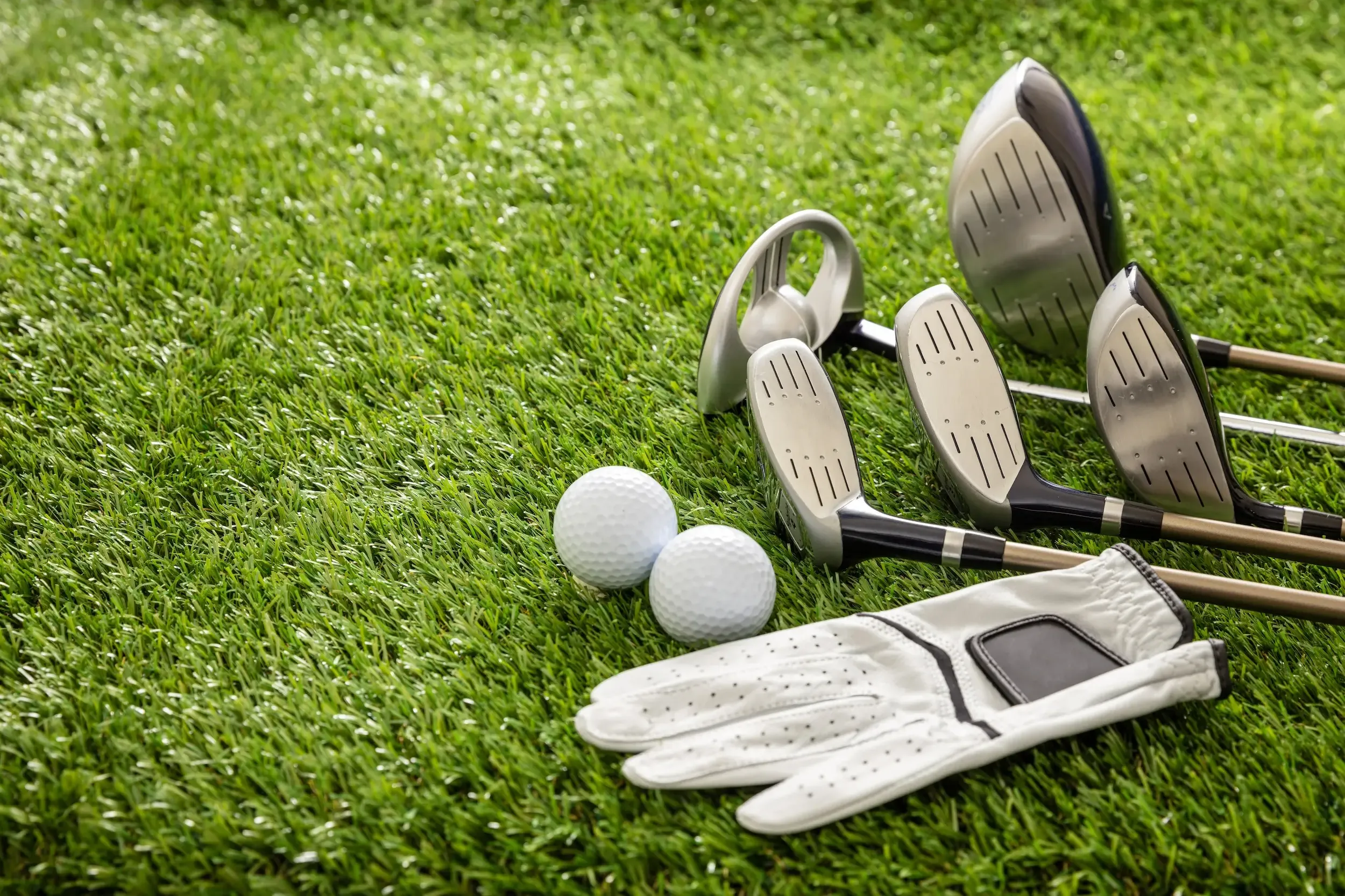 Golf gloves, golf balls, a golf club, and a ball marker placed on a green lawn