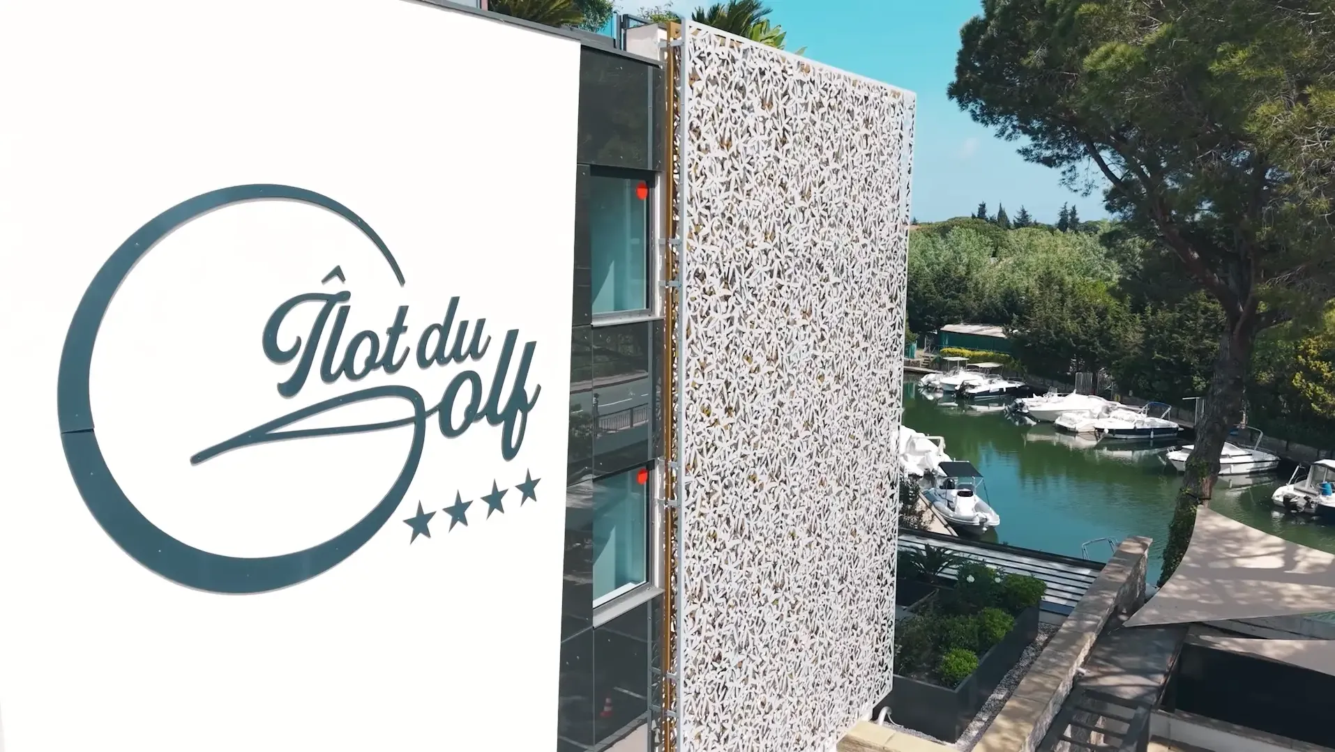 Sign with the logo and name "Îlot du Golf" and four stars near a body of water with boats