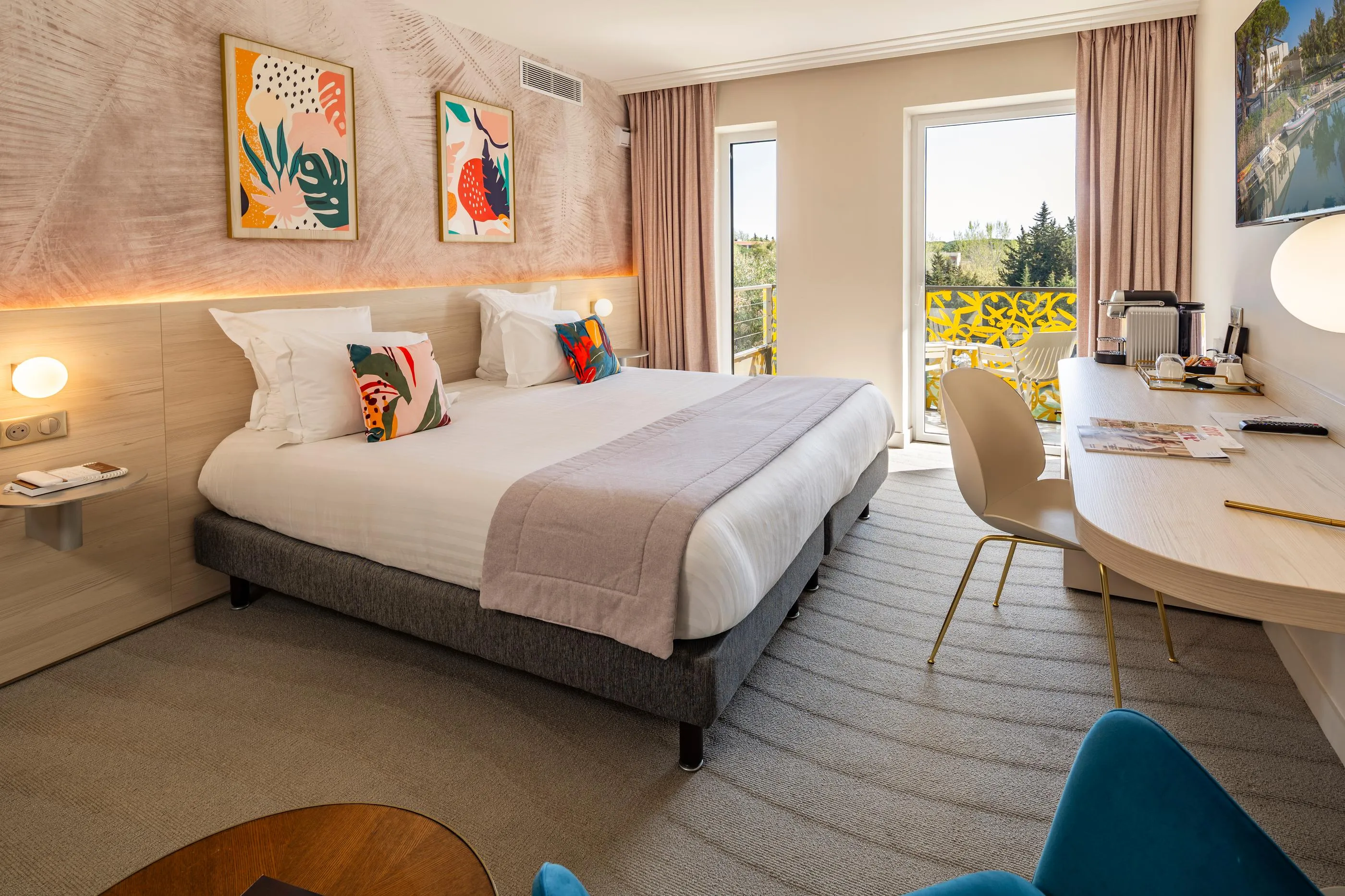 Hotel room with a bed, a work desk, wall art, and a sliding door leading to a balcony.