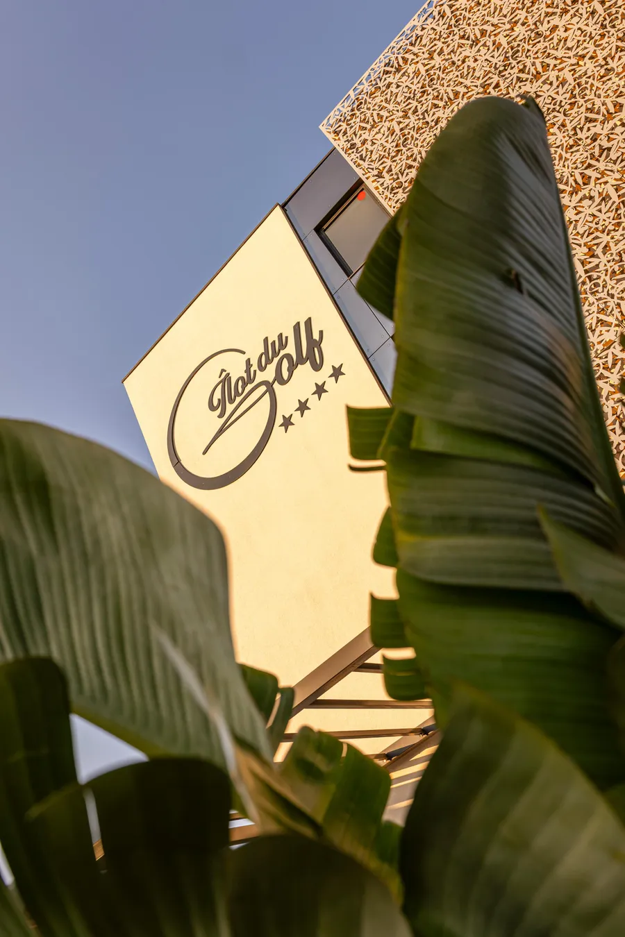 Sign with "Notre Golf" and three stars, partially obscured by green plant leaves