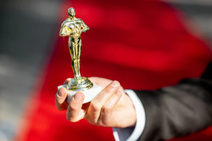 A hand holding a golden knight-shaped statuette on a pedestal against a blurred red background