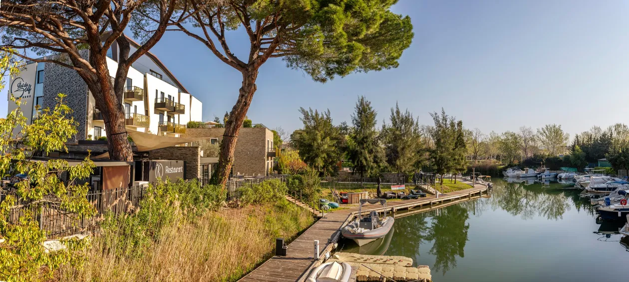 A hotel and a restaurant overlook a canal with moored boats, surrounded by trees and vegetation.