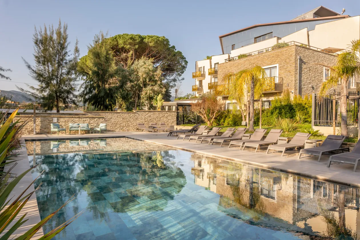 Pool surrounded by sun loungers with a stone building and trees in the background