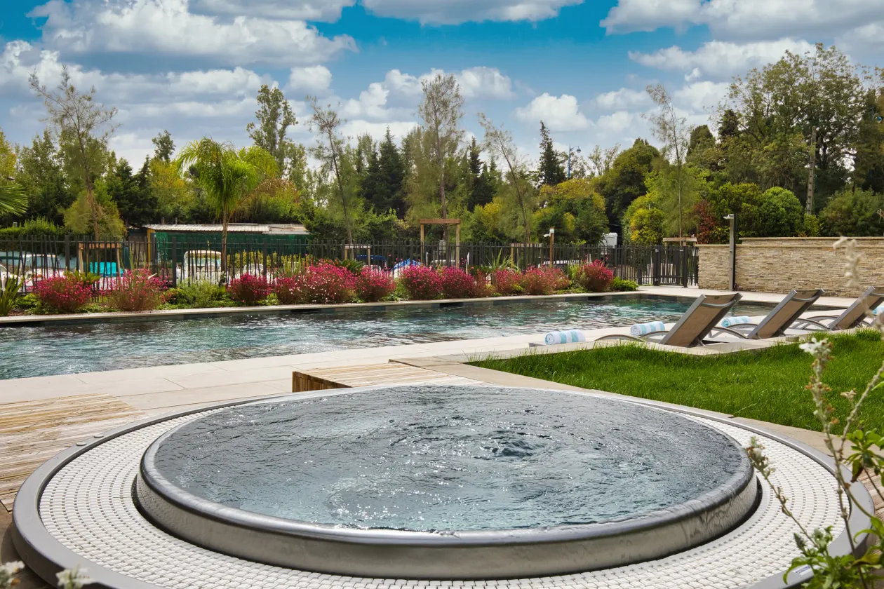 Pool surrounded by sun loungers and vegetation with a small circular basin in the foreground