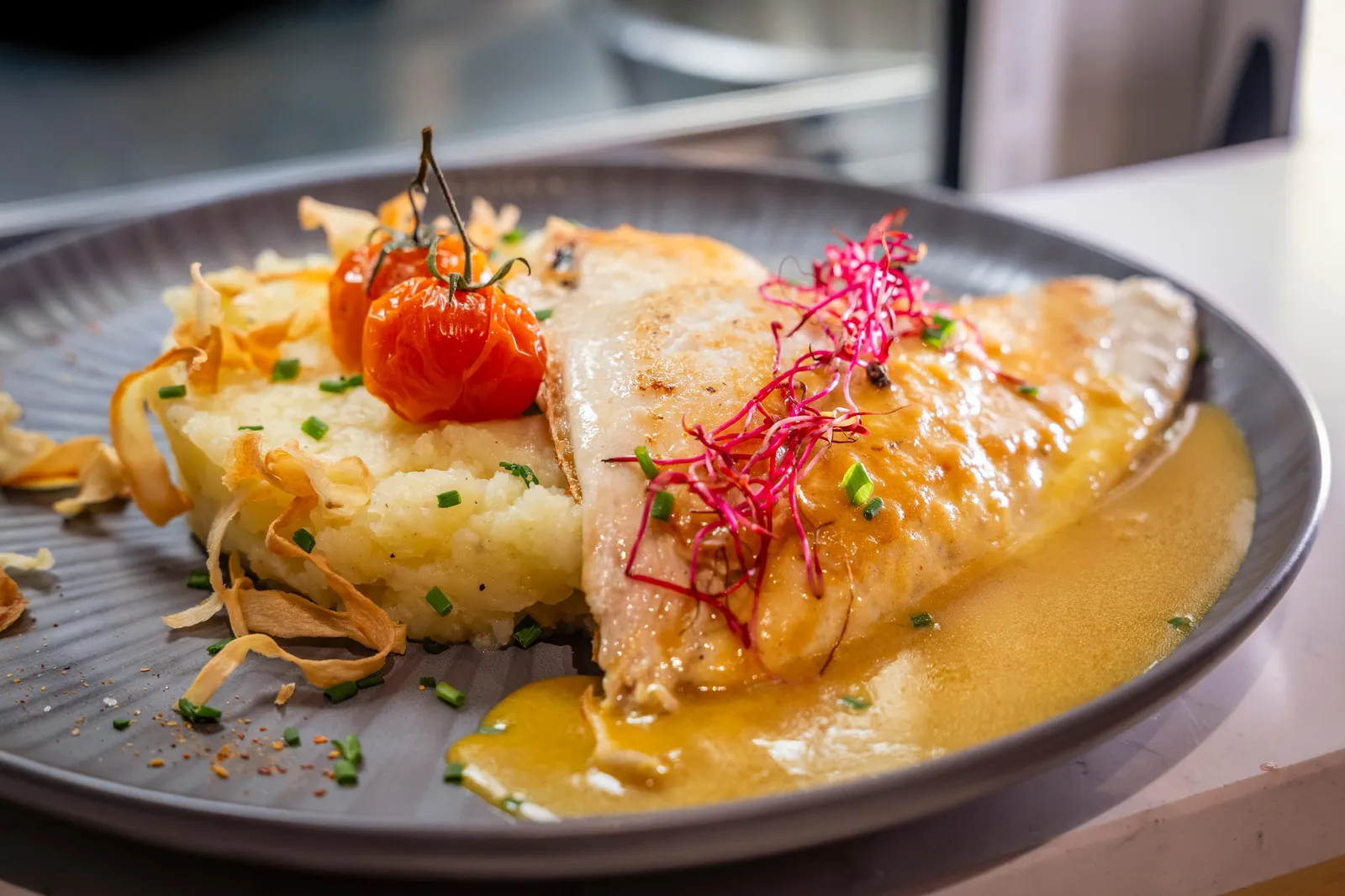 A grilled fish fillet served on a purée, accompanied by cherry tomatoes, radishes, and vegetable chips.