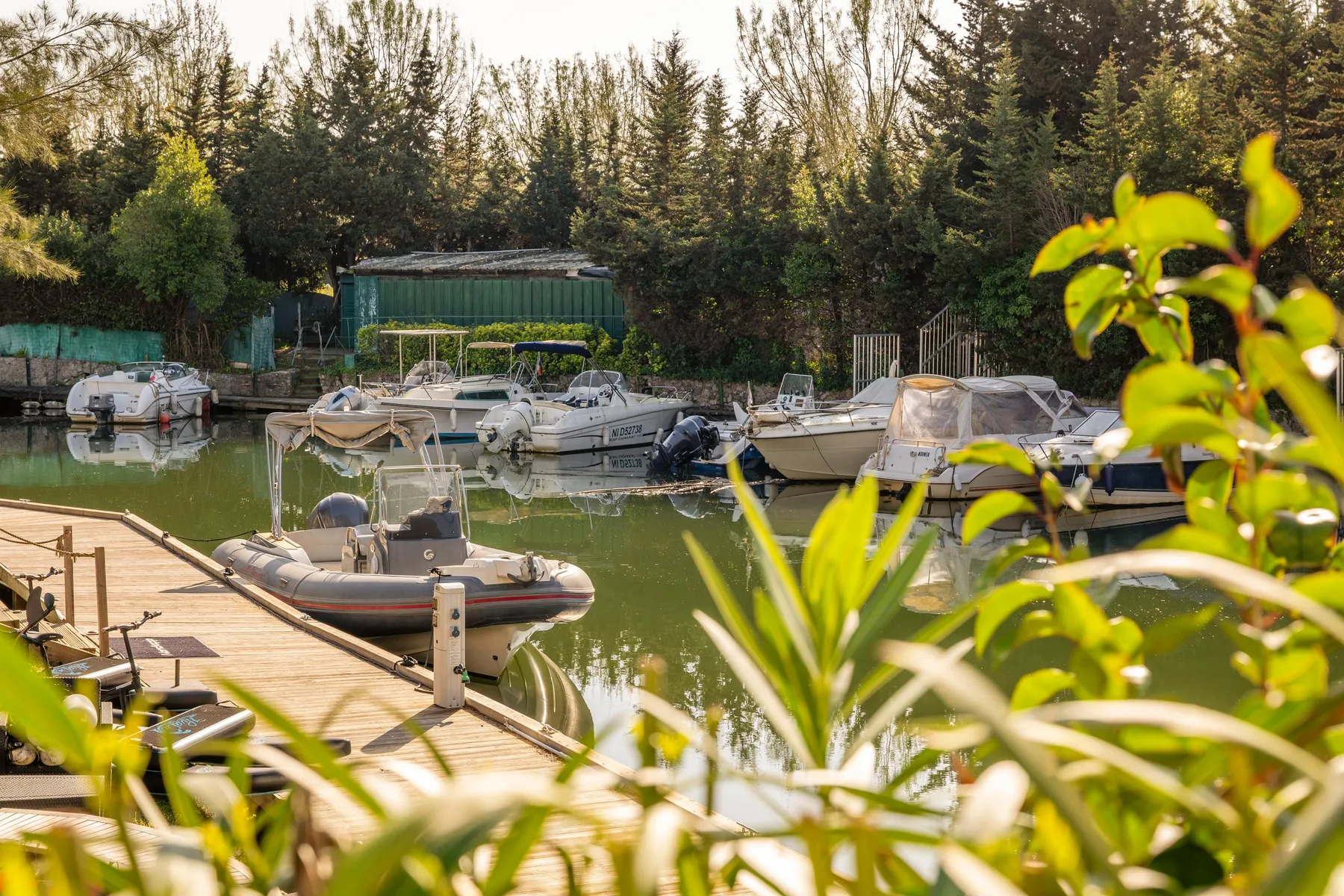 Several boats moored in a canal surrounded by trees and vegetation, with a stone jetty in the foreground.