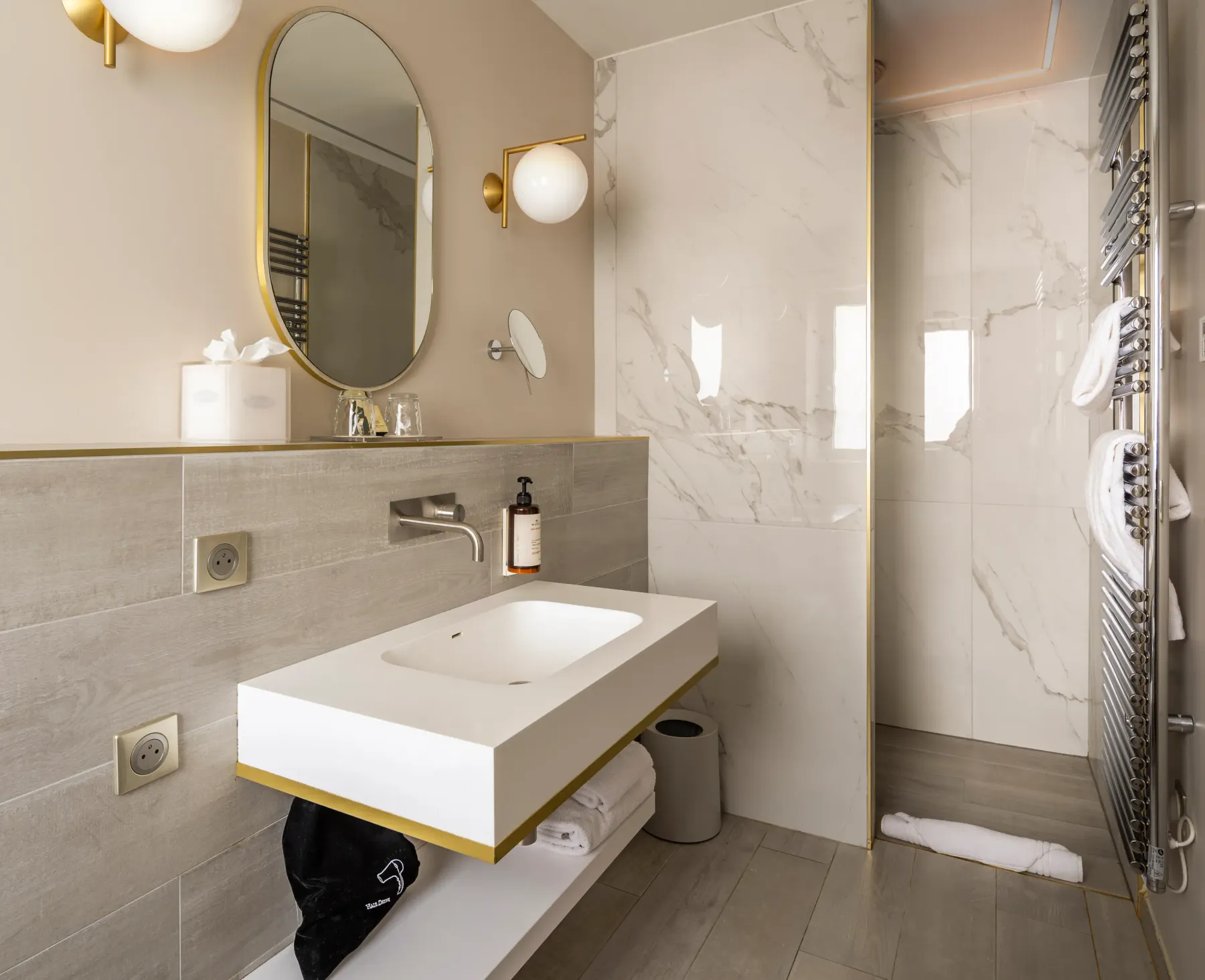 Modern bathroom with suspended sink, oval mirror, glass-doored shower, and metal accessories