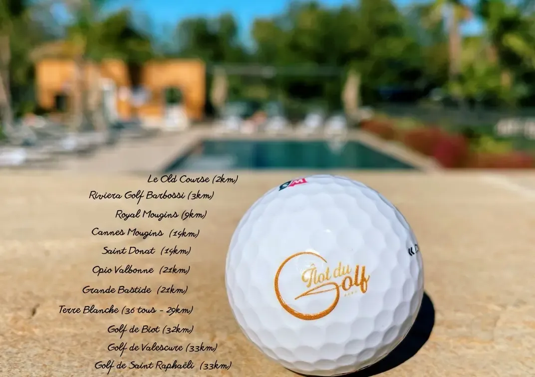 Balle de golf avec l'inscription "Golf du Domaine" devant une piscine et des bâtiments en arrière-plan