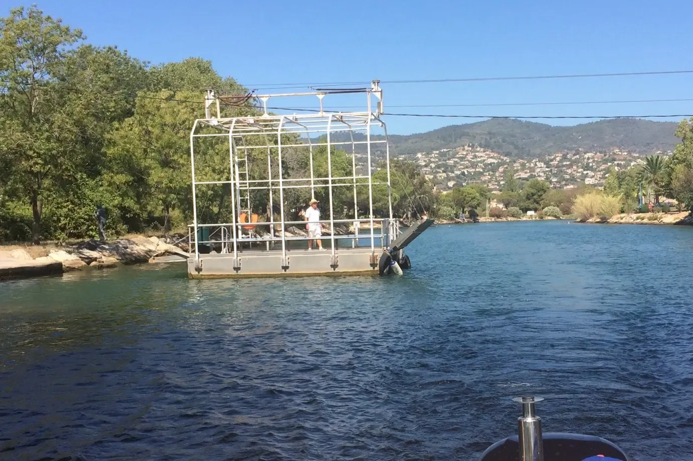 Bac à câble traversant une étendue d'eau avec des passagers et des collines boisées en arrière-plan