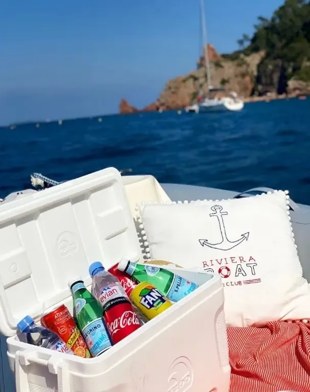 Un bac à glace rempli de bouteilles de boissons est posé sur un bateau avec une mer bleue et des rochers en arrière-plan