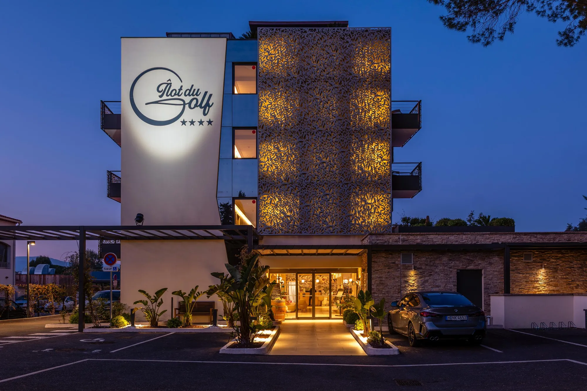 Hôtel "Plat du Golf" de quatre étoiles avec façade éclairée et entrée accessible par un chemin pavé