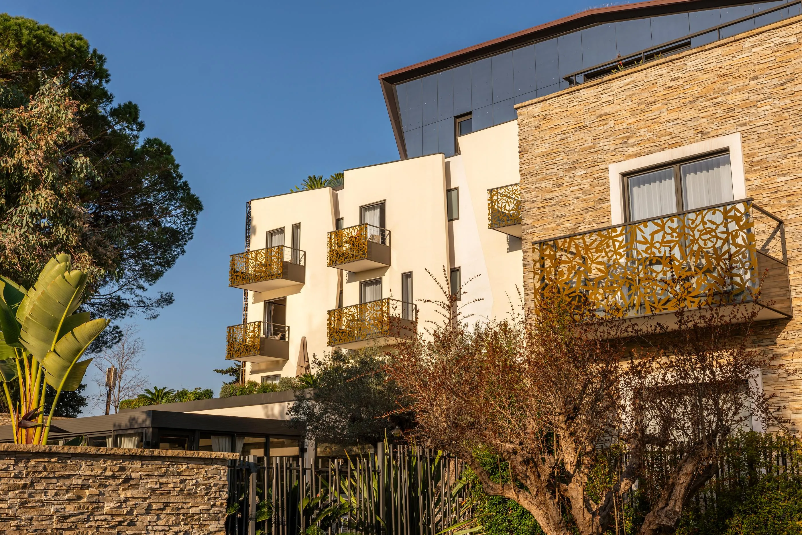 Immeuble moderne avec balcons ornés de motifs géométriques et façade en briques, entouré d'arbres et de végétation