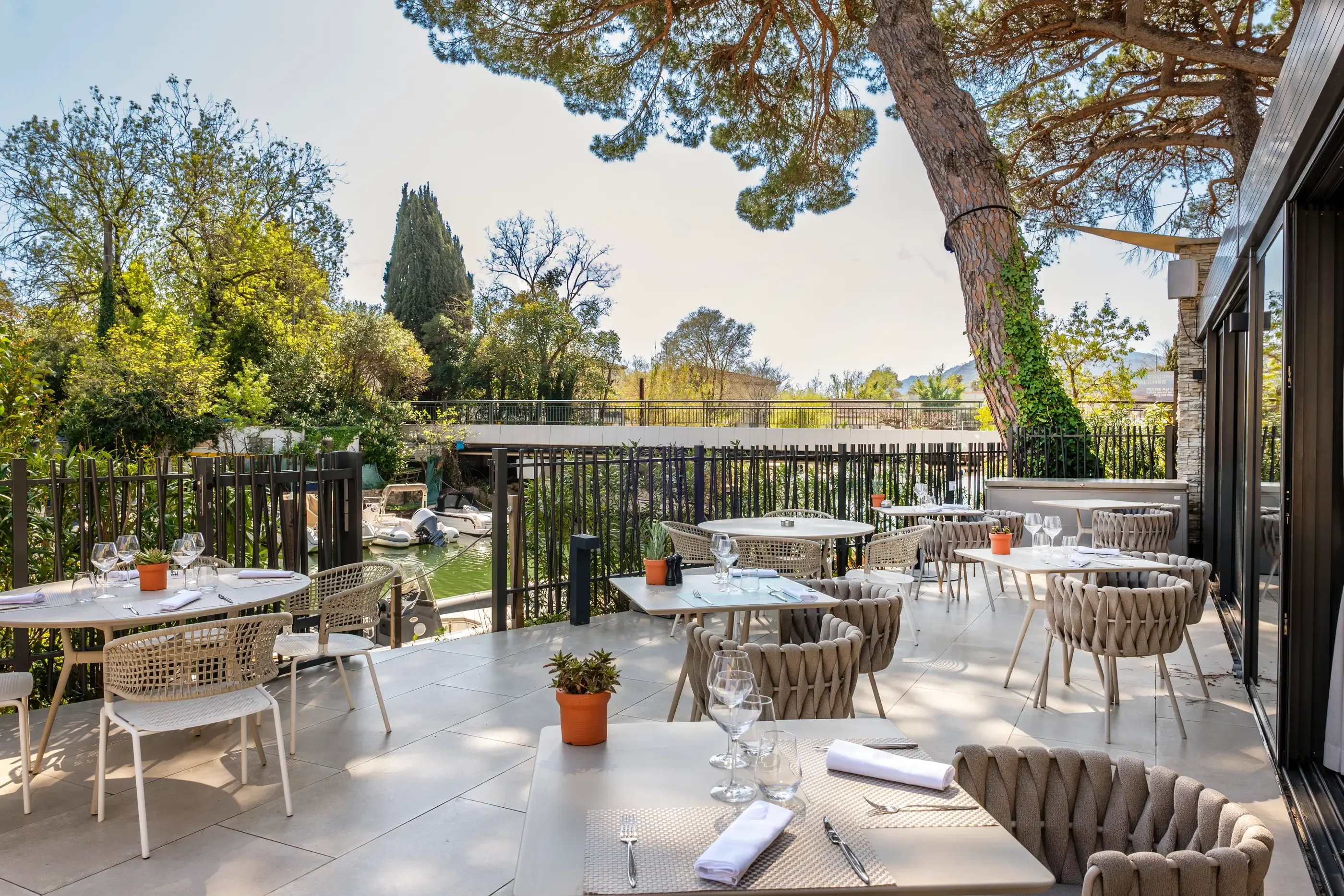 Terrasse de restaurant avec tables et chaises disposées sous une pergola, entourée d'arbres et de verdure