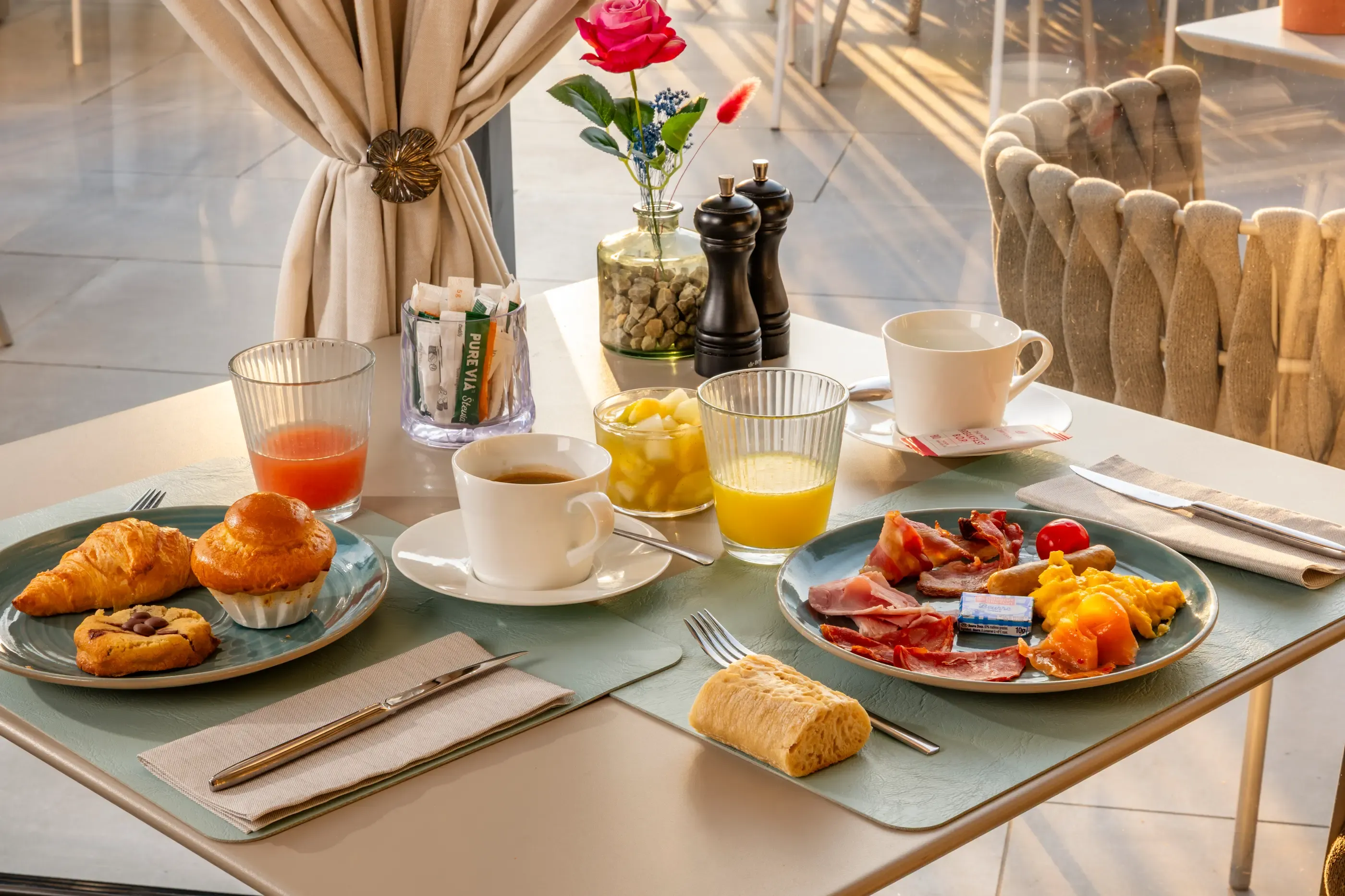 Table dressée pour le petit-déjeuner avec des croissants, des muffins, des œufs, du jambon, du fromage, des boissons et des condiments