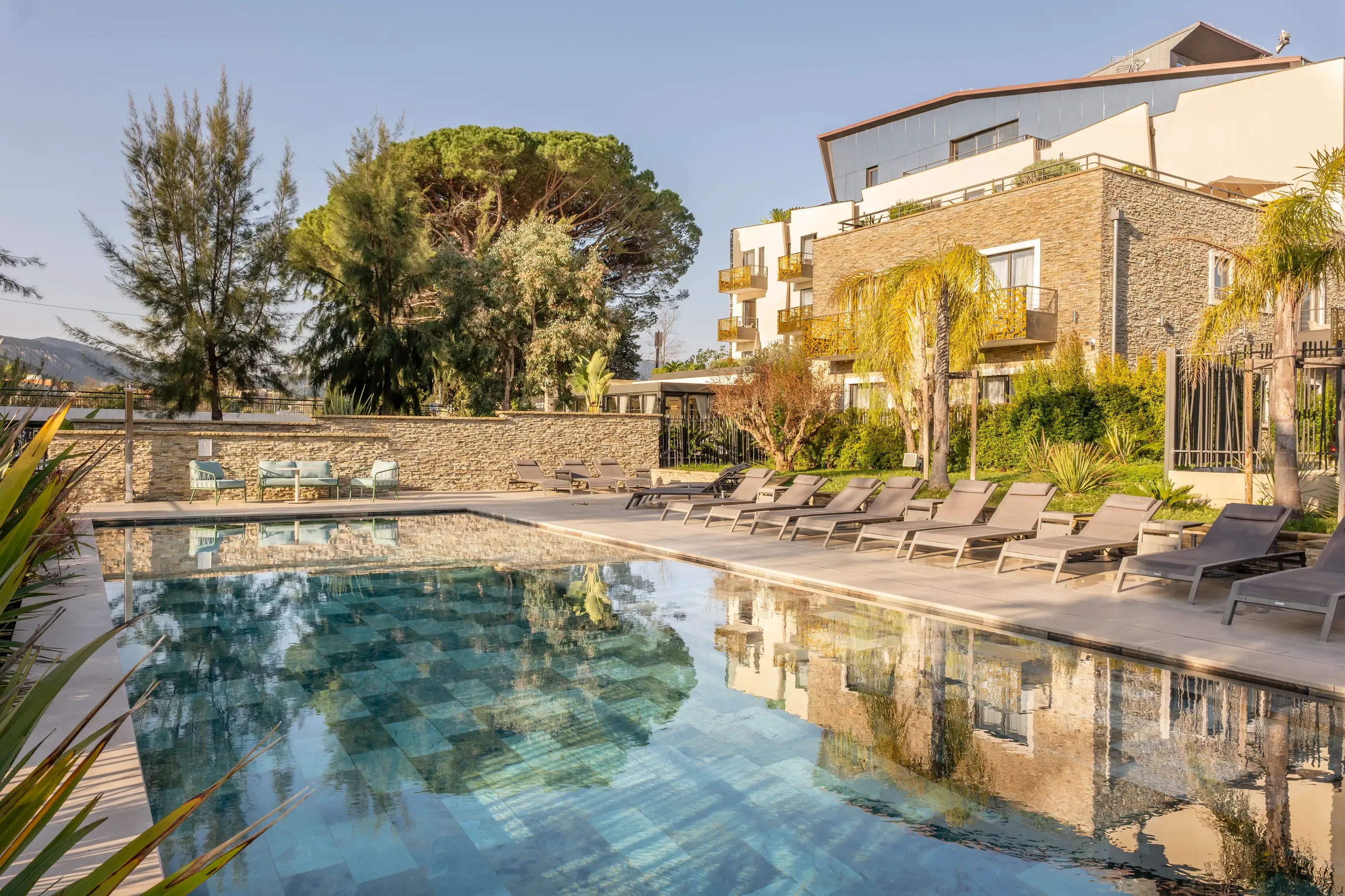 Pool surrounded by sun loungers with a stone building and trees in the background