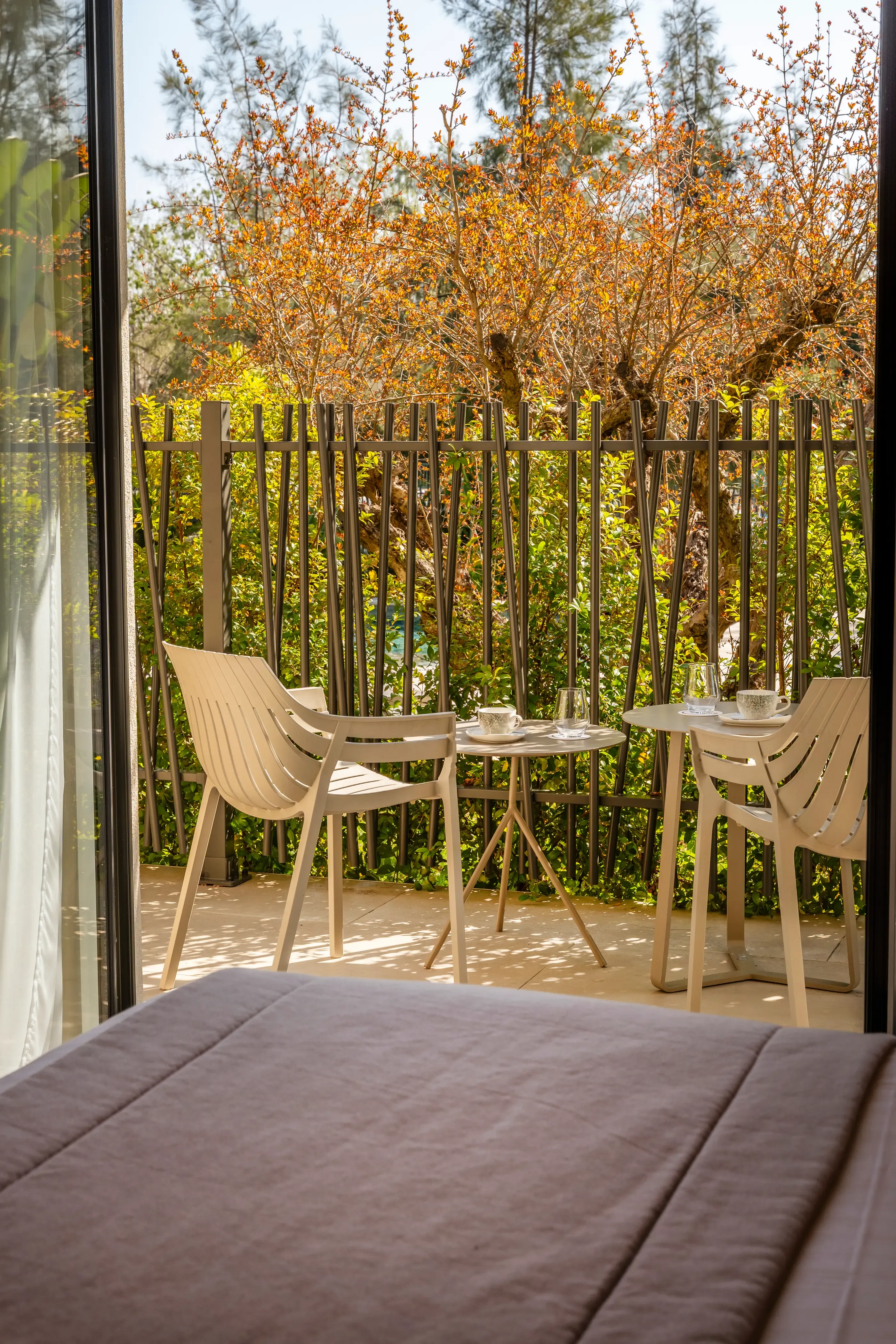 Balcon with two tables, chairs, and a view of a garden with plants and trees.