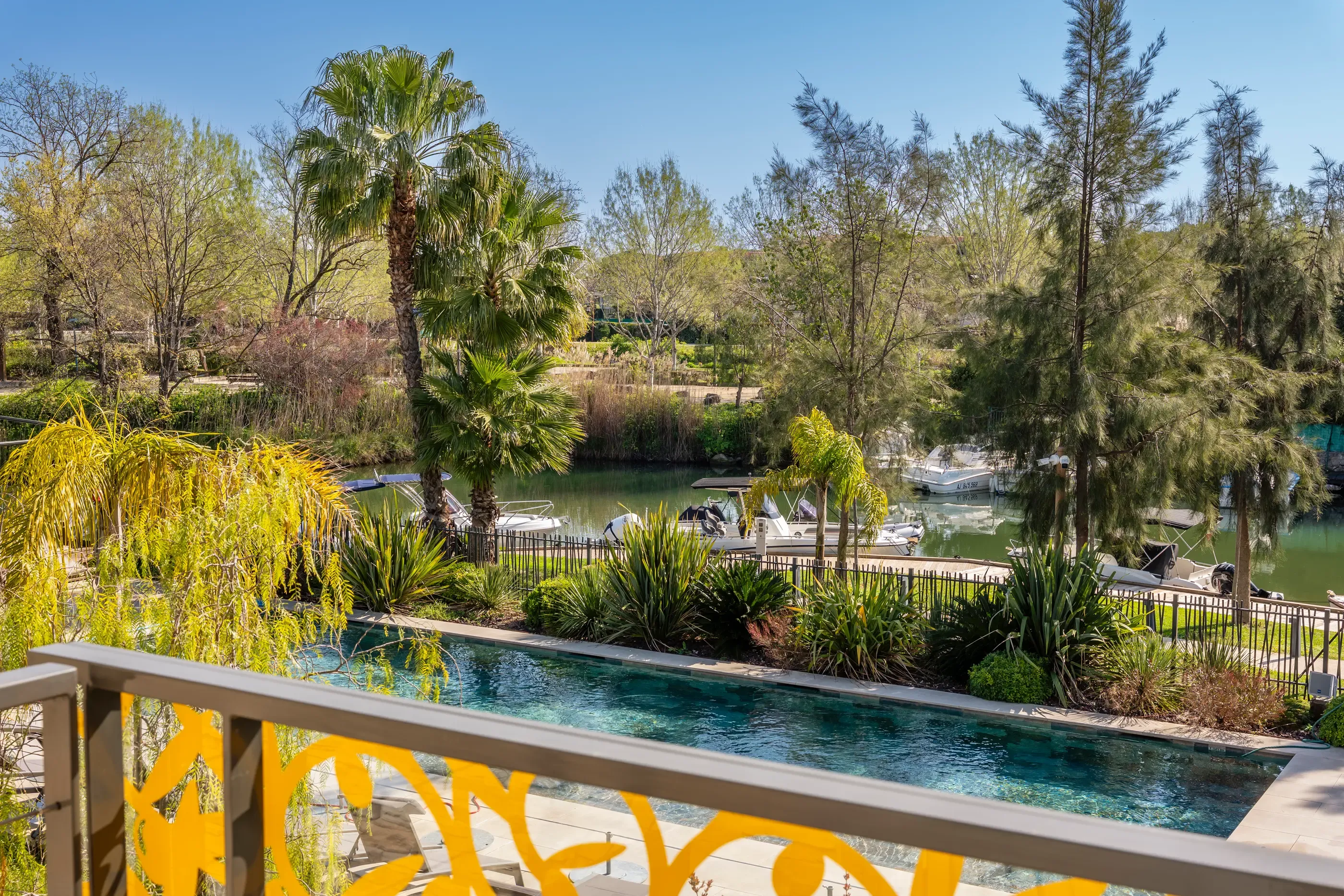 View of a lake with moored boats, surrounded by trees and vegetation, from a balcony with a pool in the foreground