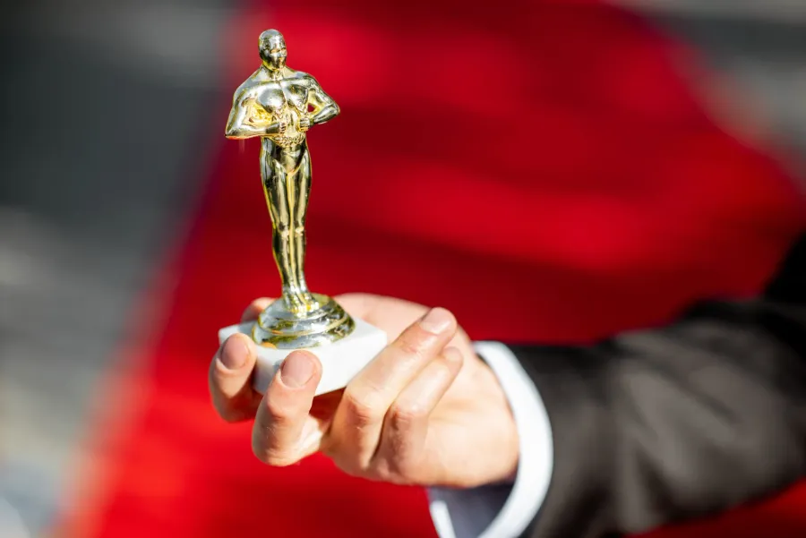 A hand holding a golden knight-shaped statuette on a pedestal against a blurred red background