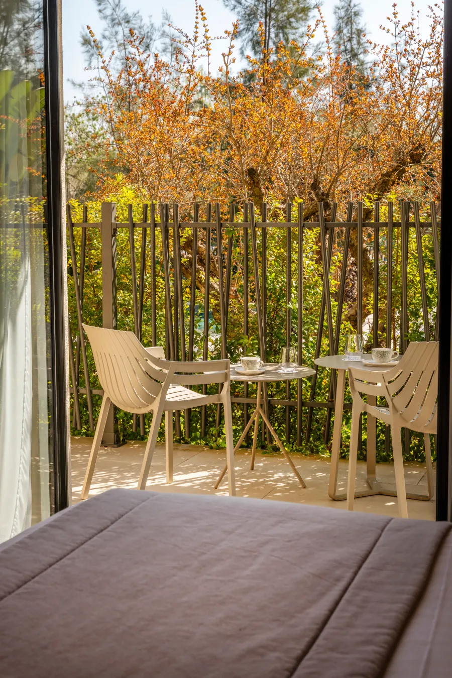 Balcon with two tables, chairs, and a view of a garden with plants and trees.